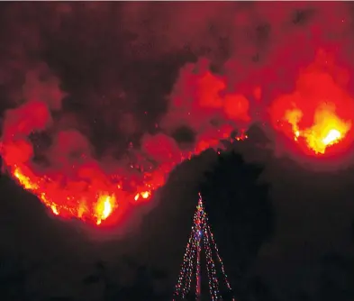  ?? MIKE ELIASON / SANTA BARBARA COUNTY FIRE DEPARTMENT VIA THE ASSOCIATED PRESS ?? A Christmas tree stands in the front yard of an evacuated home in Carpinteri­a, Calif., as wildfires burn behind it.