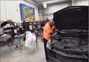  ??  ?? Hector Pereira secures a front hood on a Chevy Equinox in the body shop of Richard Chevrolet last week.