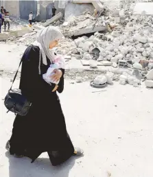  ?? — Reuters ?? A woman carrying a baby walks at the site of an air strike on a building, in Rafah.