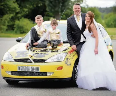  ?? Dominic Salter ?? ●● Charlotte Burgess and Tim Moore chose a yellow Ford banger as their wedding car to celebrate their mutual love of racing. With them are their children Elias (left) and Manny