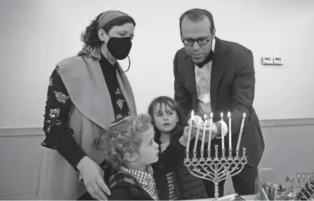  ?? NICOLAS GALINDO/THE COLUMBUS DISPATCH ?? Rabbi Stephen Slater, right, helps his son, Emet, 3, daughter, Anav, 6, light a menorah candle with wife, Bethany, at Agudas Achim Synagogue on Dec. 4.