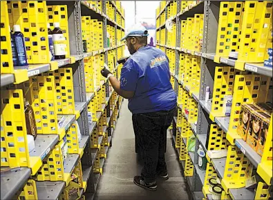  ?? Tribune News Service/Zuma Press ?? Ryan White, an Amazon employee, fills shopping bags with products for customer orders at the Amazon.com Inc. Prime Now warehouse in Los Angeles. Amazon is laying off hundreds of corporate employees in Seattle and in operations overseas.