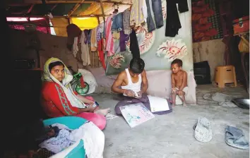  ?? Reuters ?? A man from the Rohingya community fills out an identifica­tion form provided by local police, as his wife and daughter sit next to him in their shack at a camp in New Delhi.