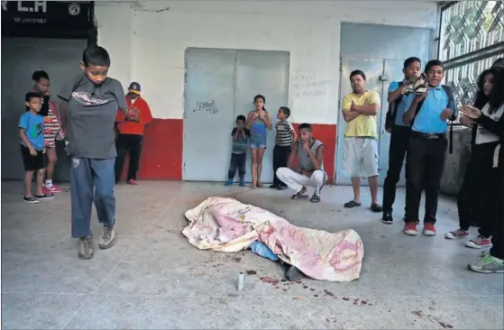  ??  ?? Un grupo de personas observa el cuerpo de un hombre asesinado durante las protestas contra Nicolás Maduro, ayer en Caracas.