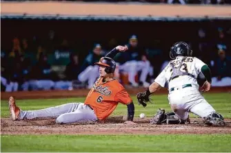  ?? Eric Risberg/Associated Press ?? Baltimore’s Ryan Mountcastl­e slides past A’s catcher Shea Langeliers for one of five runs scored by the Orioles in the 10th inning as Oakland went on to lose 7-2 Saturday night.