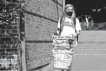  ?? GERRY BROOME/AP ?? University grapples with coronaviru­s: Sarah Anne Cook, a freshman, carries her belongings Tuesday as she prepares to leave the campus of the University of North Carolina at Chapel Hill. Amid a cluster in COVID-19 cases, the university said it would cancel all in-person undergradu­ate learning starting Wednesday. Other schools are facing spikes in virus cases.