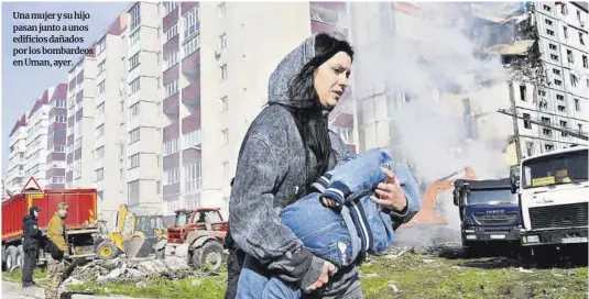  ?? Sergey Supinsky / France Presse ?? Una mujer y su hijo pasan junto a unos edificios dañados por los bombardeos en Uman, ayer.