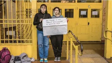  ?? SARAH PABST/THE NEW YORK TIMES ?? Agostina Fernandez Tirra, left, and Luana Pereyra, LGBTQ rights activists, hold a sign using gender-neutral language June 30 at their school in Buenos Aires, Argentina. The city bans gender-neutral language in schools.