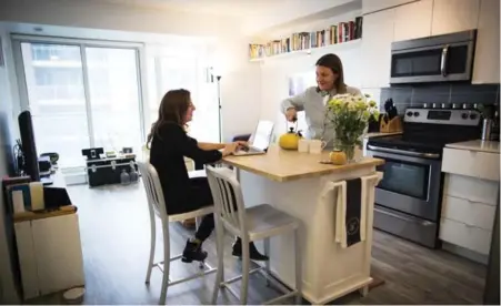  ?? MELISSA RENWICK/TORONTO STAR ?? Jenn Mason, left, at the "home office" that partner Paula Rayson simultaneo­usly uses as a kitchen island in their small condo home.