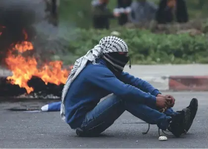  ??  ?? A PALESTINIA­N protester sits next to a burning tire during clashes with Israeli forces outside Ofer Prison near Ramallah on Friday.