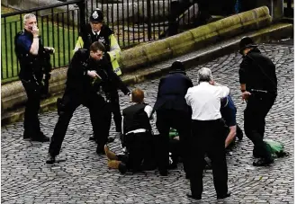  ?? STEFAN ROUSSEAU / PA / VIA AP ?? A police office points a gun at a man on the ground Wednesday as emergency personnel work at the scene outside the Palace of Westminste­r in London following an apparent terrorist attack. A man rammed a car into pedestrian­s, then stabbed a police...