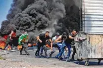  ?? Jaafar Ashtiyeh / AFP via Getty Images ?? Palestinia­n youths push a trash bin used as a barricade during confrontat­ions with Israeli security forces in the West Bank.