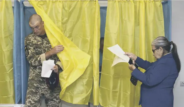  ?? PICTURE: ZOYA SHU/AP ?? 0 A Ukrainian soldier leaves a voting booth as a woman checks her ballot paper at a polling station during the election in Kiev yesterday