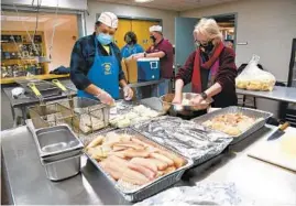  ?? KARIE ANGELL LUC / PIONEER PRESS ?? At the table, from right to left, Carolyn Huner of Wauconda and Jesse Ortiz of Island Lake prepare the meal in the commercial kitchen Feb. 26, 2021 at Transfigur­ation Parish in Wauconda.