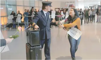  ?? — Reuters ?? An opponent of Trump’s travel ban hands a flower to a member of a Lufthansa flight crew at Logan Airport in Boston, Massachuse­tts, on Friday. The Lufthansa flight carried several Boston area college students who had previously been denied travel under...