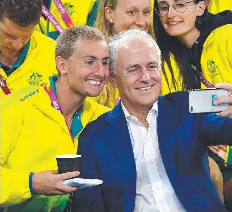  ?? Pictures: GETTY IMAGES ?? Prime Minister Malcolm Turnbull was a hit with swimmers at the Gold Coast Aquatic Centre, taking selfies with team members including Mitchell Kilduff (above), but a heavy shower found him struggling to get a poncho on in time.