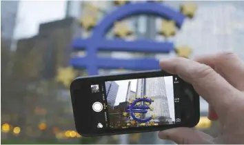  ??  ?? A man uses his mobile phone to take a picture of the euro sculpture at European Central Bank (ECB) in Frankfurt. — Reuters