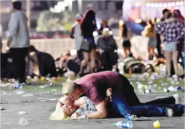  ?? — AFP photo ?? A man shields a woman with his body as others flee the Route 91 Harvest country music festival grounds during the shooting.