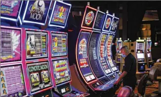  ?? JOHN LOCHER / ASSOCIATED PRESS ?? A worker looks over a slot machine in May, with chairs removed from some to keep social distancing at closed Caesars Palace in Las Vegas. Casinos began reopening Thursday.