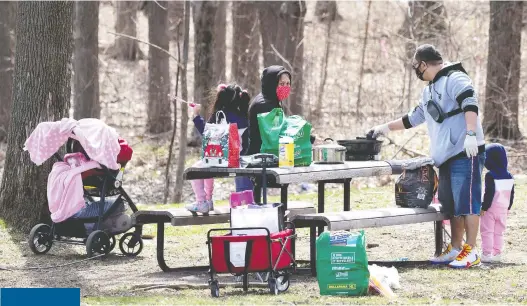  ?? ALLEN MCINNIS ?? A family keeps their face masks on as they prepare for a family picnic in a quiet corner of Mount Royal Park on Sunday.