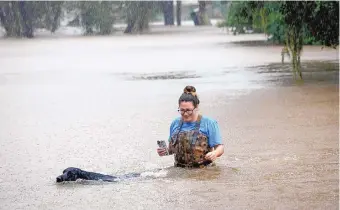  ?? STEVE GONZALES/HOUSTON CHRONICLE ?? Adelle Puma and her dog “Ridge” make their way from the submerged Mary Xing bridge over Marys Creek as Tropical Storm Beta rainfall trained over the area Tuesday in Friendswoo­d, Texas.