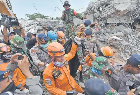  ??  ?? Members of a search and rescue team carry the body of a quake victim in Bangsal, north Lombok. — AFP photo