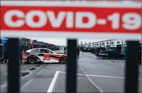  ?? (AP/Matt Slocum) ?? Crew members are visible under a covid-19 alert sign as they push the car of Christophe­r Bell through the garage area before a scheduled NASCAR Cup Series race in June at Pocono Raceway in Long Pond, Pa. NASCAR will not grant covid-19 relief during the playoffs, which means a positive coronaviru­s test will end a driver’s championsh­ip bid.