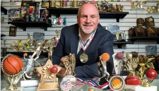  ?? Tribune News Service ?? n Keith Baldwin, 58, chief relationsh­ip officer for Spike’s Trophies, poses for a portrait surrounded by participat­ion trophies on the counter. Baldwin participat­ed in a triathlon recently and made a participat­ion medal (like the one hanging around his...