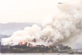  ?? — AFP photos ?? A military helicopter flies above a burning woodchip mill in Eden, in Australia’s New South Wales state.