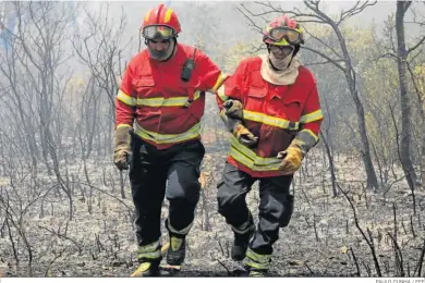  ?? PAULO CUNHA / EFE ?? Dos bomberos portuguese­s se retiran cansados de un terreno completame­nte quemado en Freixianda.