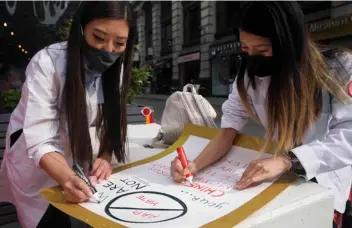  ?? AP Photo/Bebeto Matthews ?? Dr. Michelle Lee (left) a radiology resident, and Ida Chen (right) a physician assistant student, prepare posters they carry at rallies protesting anti-Asian hate, on April 24 in New York’s Chinatown.