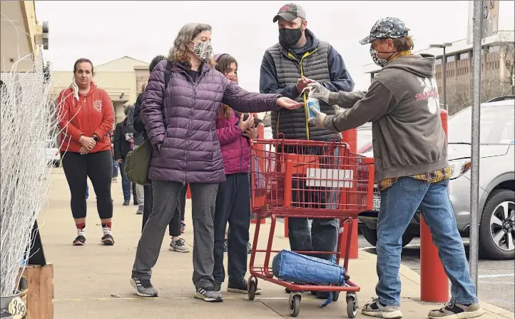  ?? Photos by Lori Van Buren / Times Union ?? A Trader Joe's employee offers hand sanitizer to customers entering the store on Friday in Colonie. The company will pay its employees “thank you pay” through at least the end of March.