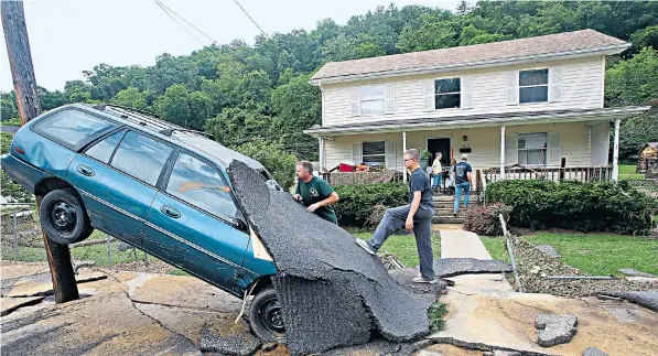 ??  ?? Above, Jay Bennett and his stepson Easton Phillips study a neighbour’s car swept up by flooding in White Sulphur Springs, West Virginia; left, neighbours in White Sulphur Springs hug as they clean up after the flood; right, a car rests on the bank of a...