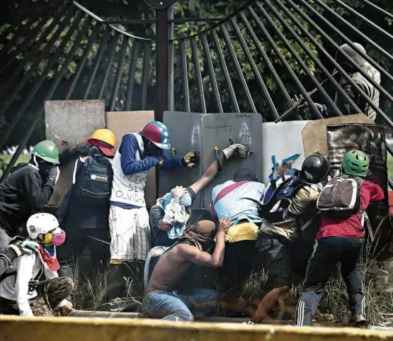  ?? Juan Barreto-31.mai.2017/AFP ?? Manifestan­tes se protegem da Guarda Nacional venezuelan­a em Caracas em maio; pelo menos 125 pessoas morreram em protestos no país neste ano