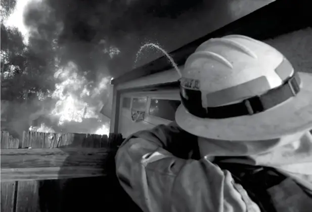  ?? (AP Photo/Chris Carlson) ?? A Los Angeles County firefighte­r puts water a burning house in a wildfire in the Lake View Terrace area of Los Angeles Tuesday, Dec. 5, 2017. Ferocious winds in Southern California have whipped up explosive wildfires, burning a psychiatri­c hospital and...