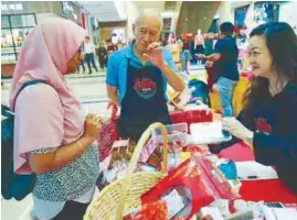  ??  ?? Hariz (centre) and Syahrain (right) showing some food items to a customer. – ASYRAF RASID/THESUN