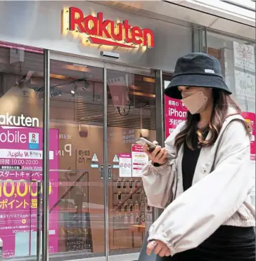  ?? ?? Financial strain: A woman walks past a mobile shop of the ecommerce firm in Tokyo. Rakuten’s move to issue bonds may signal a delay in raising funds through the listing of its banking and securities units. — AFP