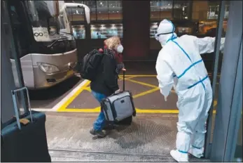  ?? Airport. ?? A passenger is directed to a bus by an Olympic worker wearing protective gear Monday at the Beijing Capital Internatio­nal