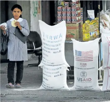  ?? LEFTERIS PITARAKIS/THE ASSOCIATED PRESS FILES ?? A Palestinia­n pupil walks past sacks of flour, some part of humanitari­an aid by United Nations Relief and Works Agency, (UNRWA), and USAID, but now offered for sale by a vendor outside a food store in Shatie refugee camp, in Gaza City. U.S. President...