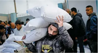  ?? AFP-Yonhap ?? A Palestinia­n man carries sacks of humanitari­an aid at the distributi­on center of the United Nations Relief and Works Agency for Palestine Refugees (UNRWA), at Rafah in Gaza Strip, March 3, amid the ongoing conflict between Israel and the Hamas movement.