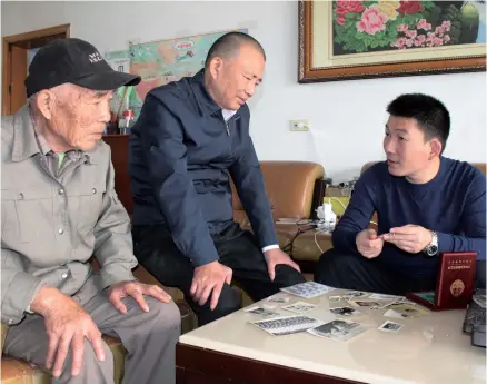  ??  ?? Three retired soldiers, Xu Zhiwen, Xu Jian and Xu Jiaping (from left to right) look at black and white pictures that were taken when they were in the military. Ten members in three generation­s of the Xu family have served their country in the military. — Yang Yang