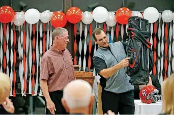  ?? PHOTO BY BRYAN TERRY, THE OKLAHOMAN ?? New Carl Albert football coach Mike Corley presents retiring coach Gary Rose with a golf club bag during a retirement party for Rose. Corley will be just one of many new faces on high school football sidelines next season.