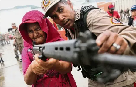  ??  ?? Eye on the target: A member of the Militia of the National Bolivarian Armed Forces teaching a woman how to use a rifle during a military exercise in Caracas. — Reuters