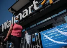  ?? Andrew Caballero-Reynolds, AFP/Getty Images ?? A woman wearing a mask walks past a sign informing customers that face coverings are required in front of a Walmart store in Washington on Wednesday.