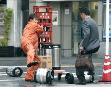  ?? Kyodo News/Associated Press ?? A worker reacts after canisters fall from a carriage due to strong wind in Tokyo on Monday. A powerful typhoon made landfall in central Japan Monday morning after washing three American airmen in Okinawa out to sea the previous day, killing at least...