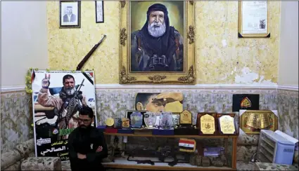  ??  ?? In this Dec. 5 photo, a man sits among awards, certificat­es of appreciati­on and posters belonging to the sniper Ali Jayad al-Salhi, 65, a volunteer with Popular Mobilizati­on Forces killed fighting Islamic State militants, in Basra, 340 miles southeast...