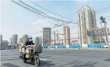  ?? /Bloomberg ?? In suspension:
A delivery driver wearing a protective mask travels along a road past an idle constructi­on site in Shanghai, China, on February 27. China is gradually getting back to work, but the economy is still operating far below capacity.