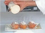  ??  ?? Chef Erik Mahr sprinkles powdered sugar over beignets garnished with orange syrup.