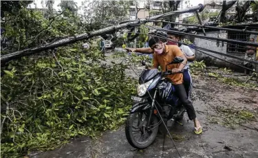  ?? Bikas Das / Associated Press ?? People make their way through downed cables and a fallen tree branch after Cyclone Amphan hit in Kolkata, India. More than 80 people have died and thousands are without access to fresh water and electricit­y.