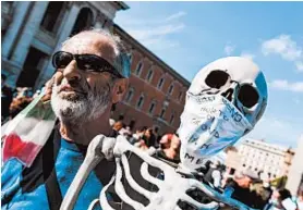  ?? ANDREAS SOLARO/GETTY-AFP ?? A protester holds a reproducti­on of a human skeleton Saturday in Rome. The mask says, “I did not die of coronaviru­s but of hunger.”